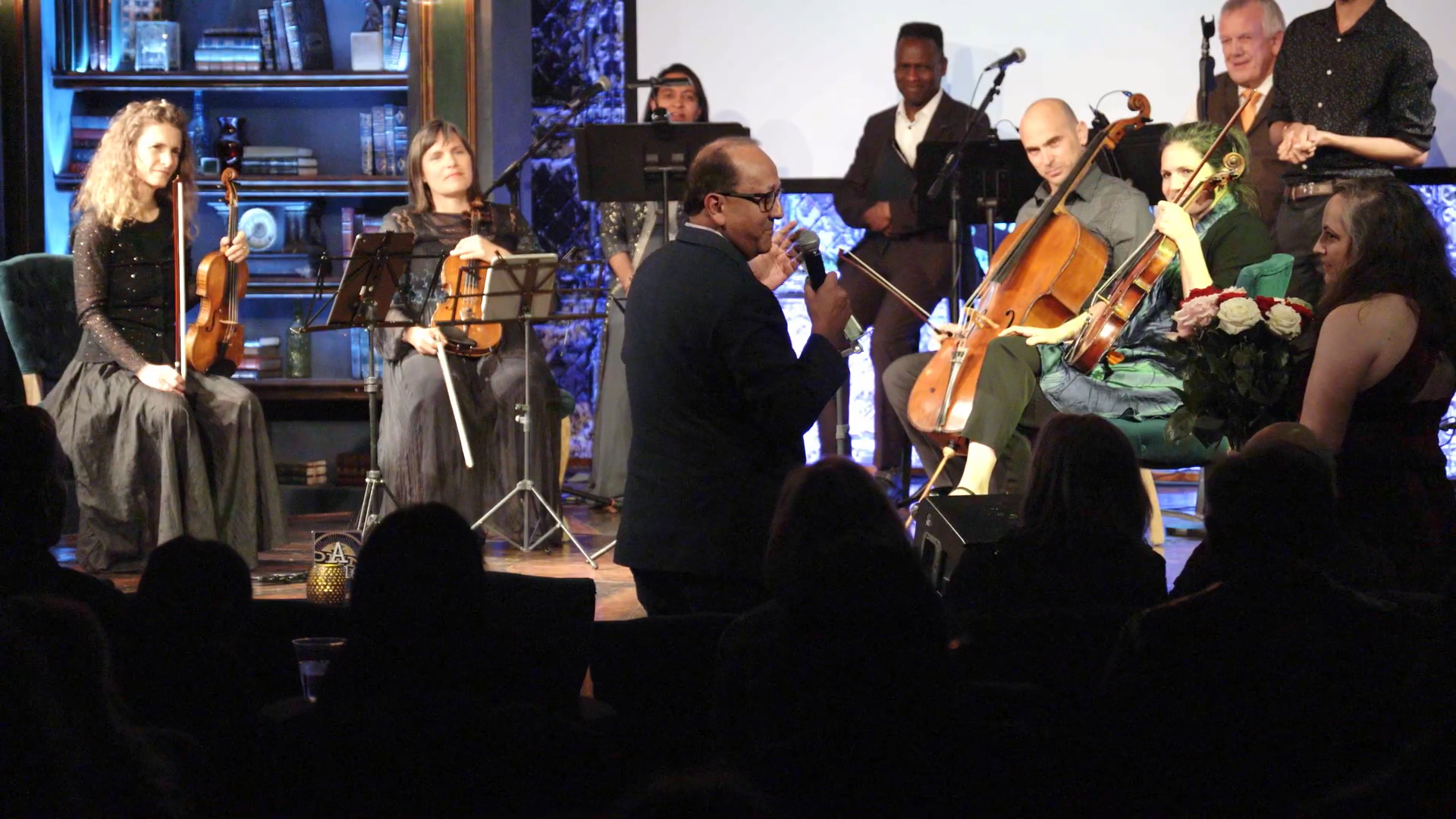 Dean Rashid Bashir standing in front of the stage. A woman on the right is holding several long-stemmed roses.