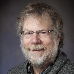 Photo shows headshot of man with beard and glasses